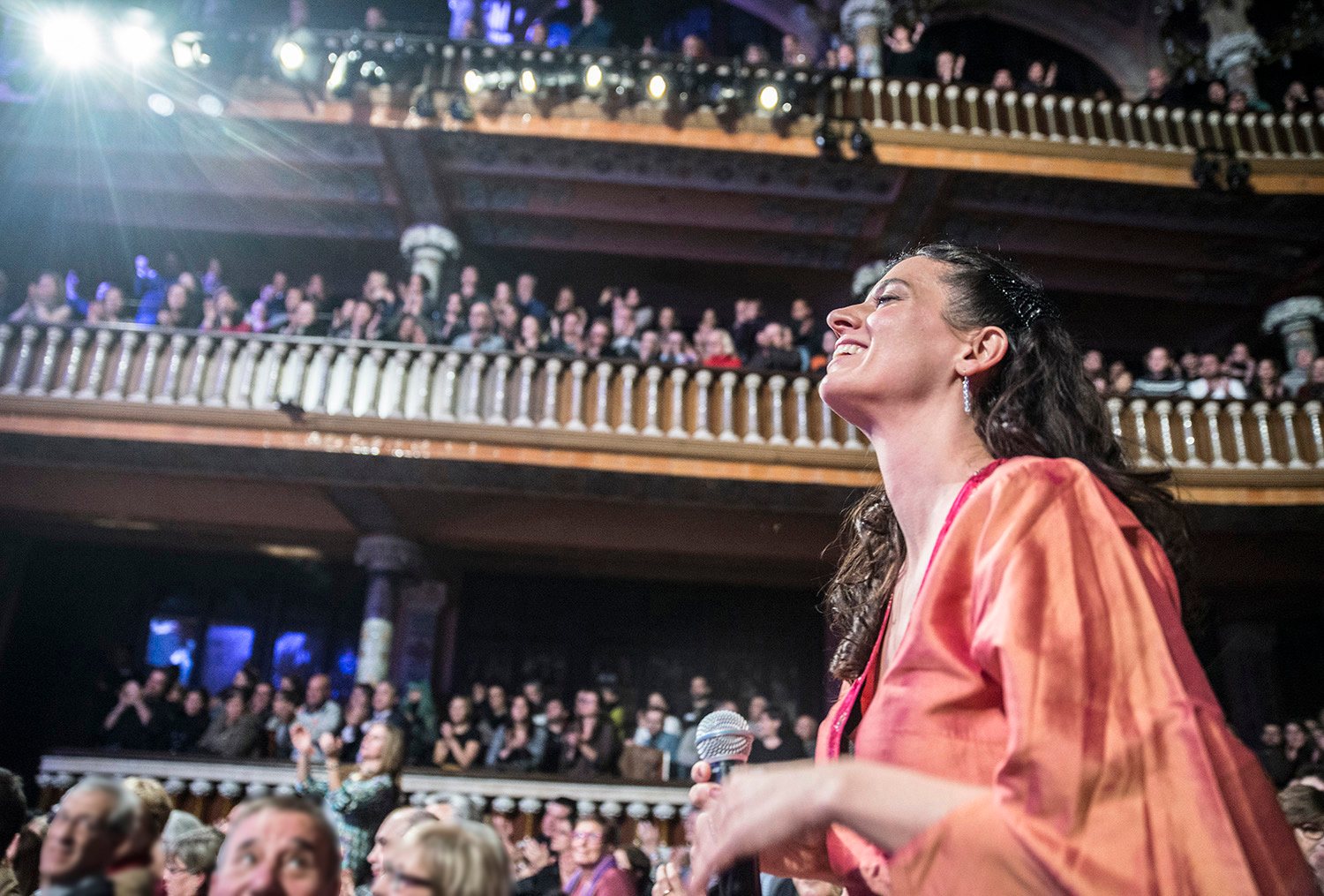 Cumie, microphone in hand, smiling up at a full house from the stalls of the Palau de la Música Catalana.